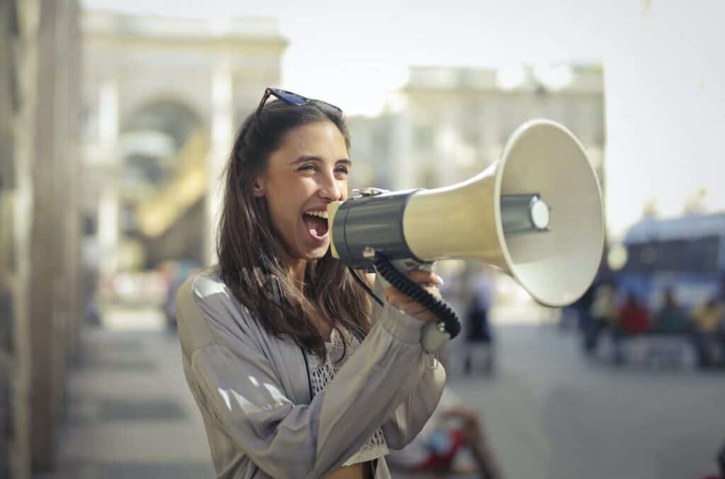 A young woman passionately shouting into a megaphone while engaging in online German learning.