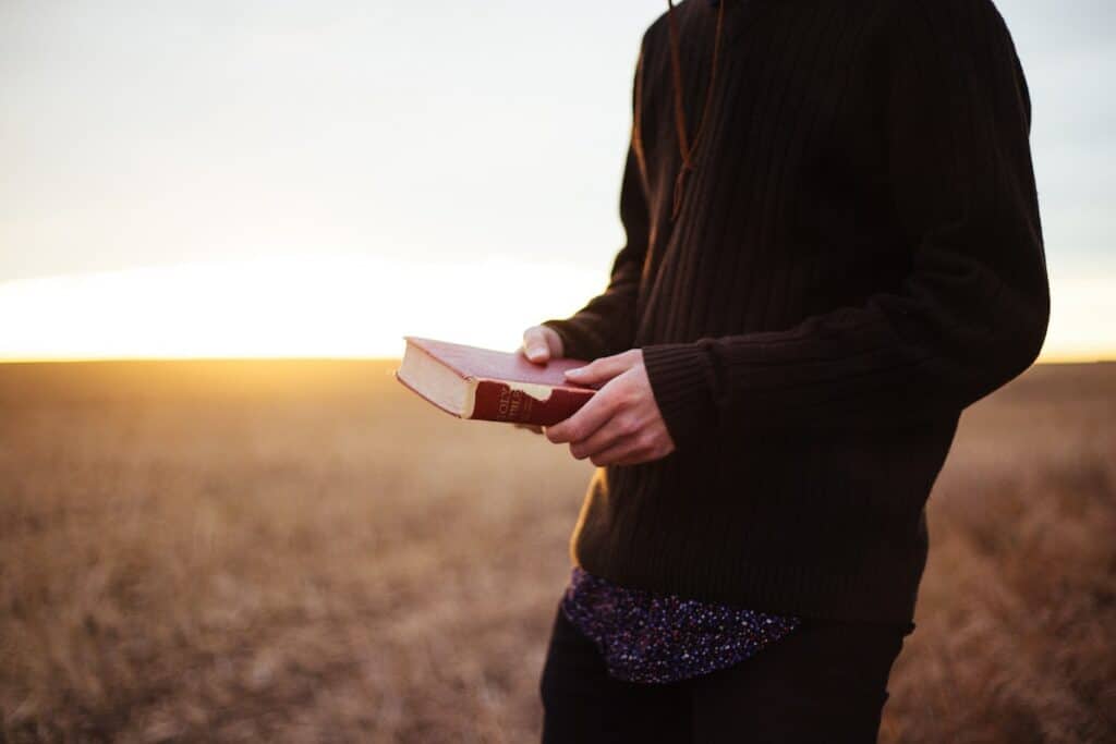 A man holding a bible while learning German online in a field at sunset.