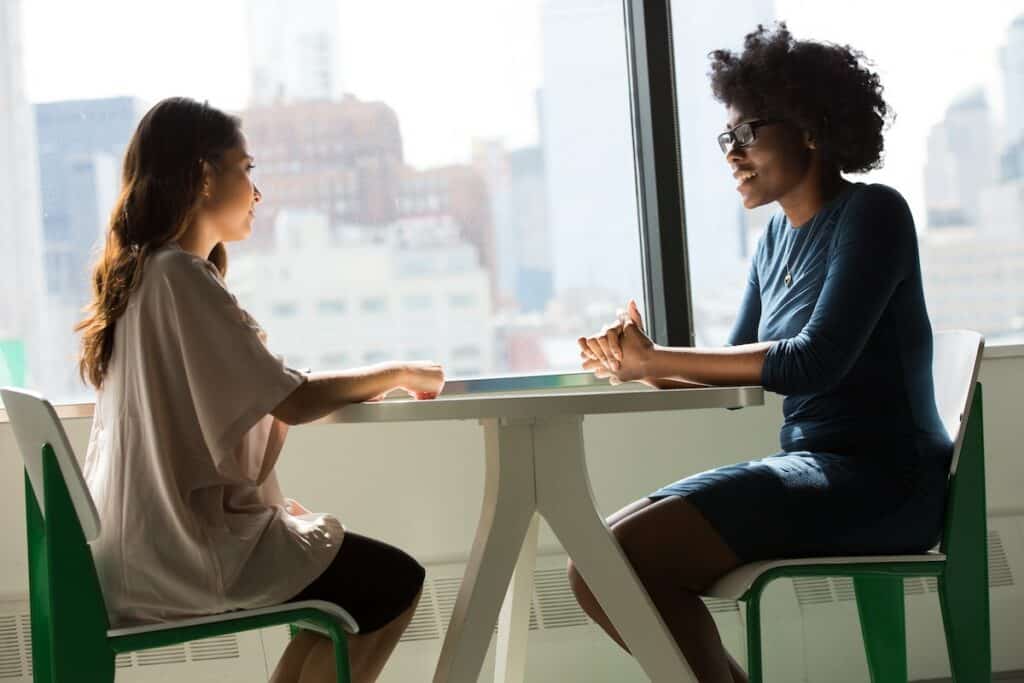 Two women are engaged in a conversation at a table in an office while discussing their progress in learning German.