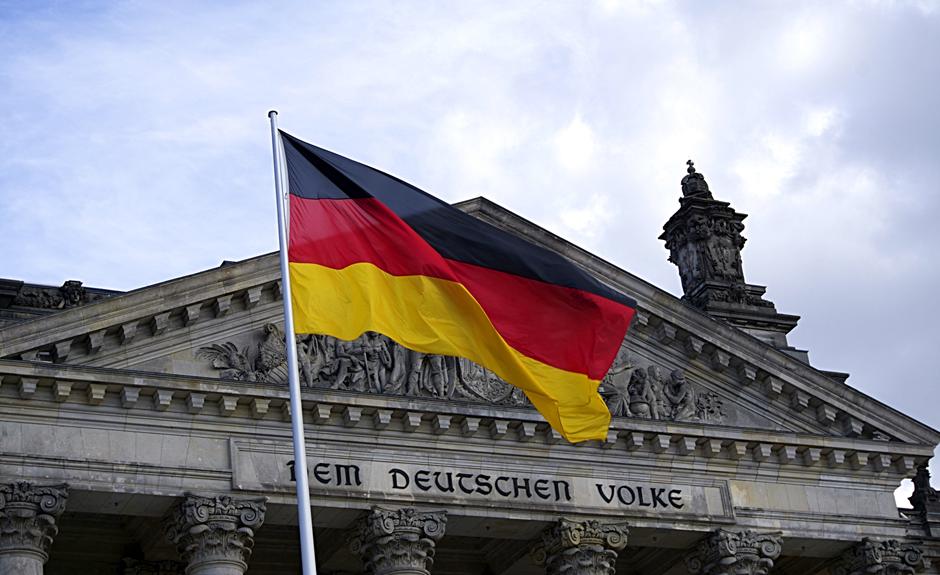 A German flag is fluttering in front of a building, providing visual inspiration for those eager to learn German online.