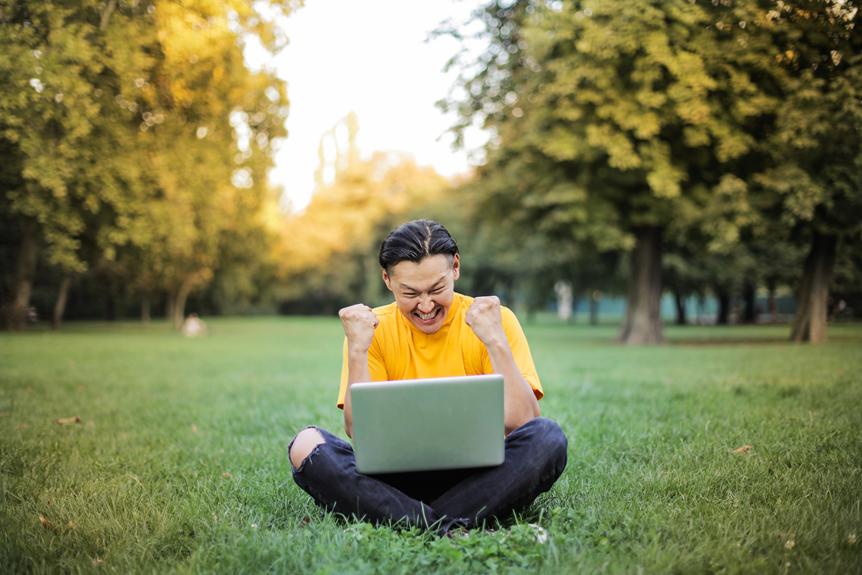 A young man learning German online, sitting on the grass with a laptop.